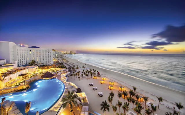 Piscina iluminada al atardecer en un hotel solo para adultos frente al mar en Cancún